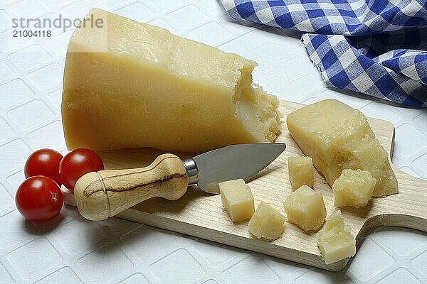 A piece of Parmesan cheese and chopped pieces of cheese on a wooden board