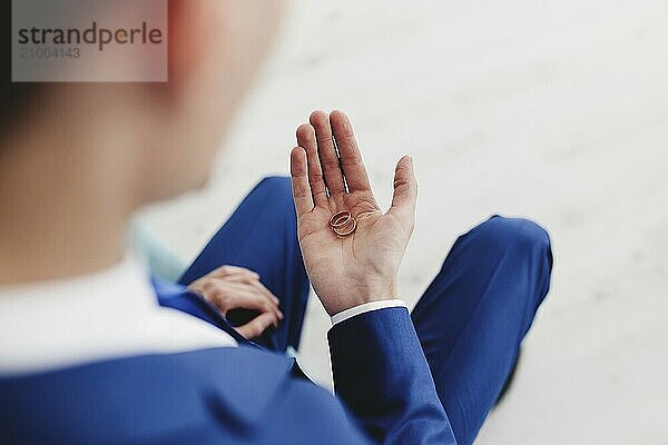 Groom in blue suit holds wedding rings in his hand.