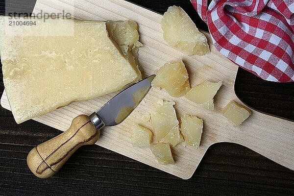 A piece of Parmesan cheese and chopped pieces of cheese on a wooden board