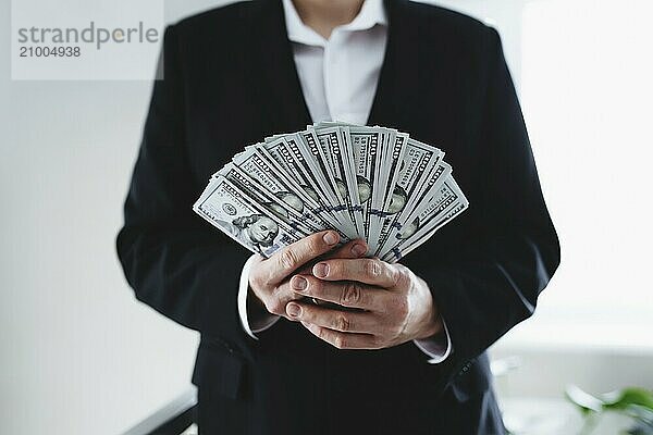 One hundred dollar bills money fun  in hand of man in suit and white shirt. Blurred background.