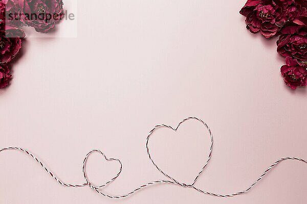 Valentine card. Heart shapes. Red white string or rope. Roses. Pink background.