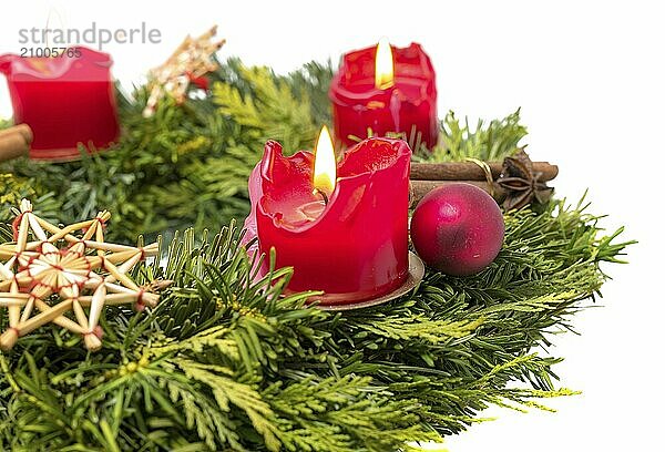 Decorated Advent wreath made of fir branches with burning red candles on a white background