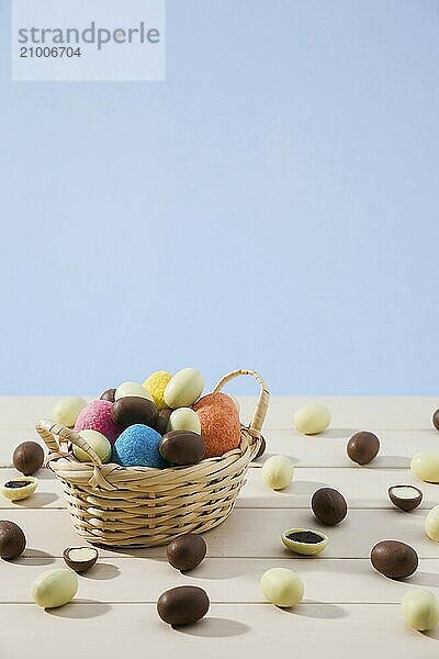 Easter chocolate eggs in a small basket and some small eggs over a white table with blue background