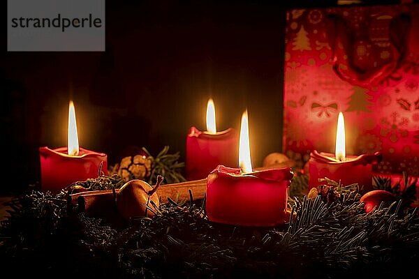 Decorated Advent wreath made of fir branches with burning red candles against a black background