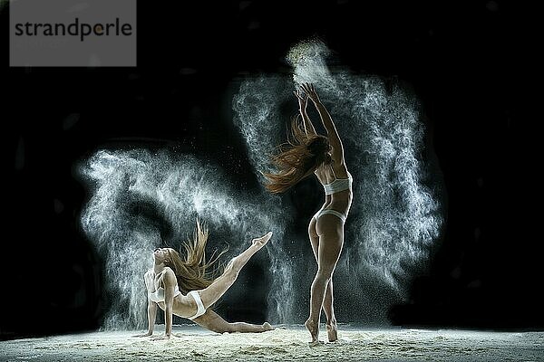 Young girls dancing in a cloud of white dust in studio on black background