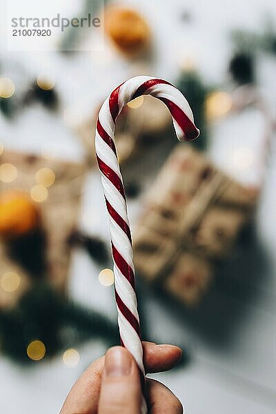 Christmas gifts  hand holds lollipop  tangerine on white wooden background.