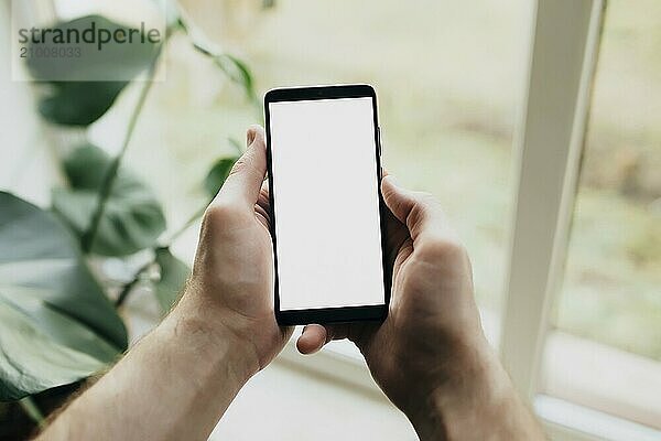 Man is holding smartphone with white screen. Blurred background.