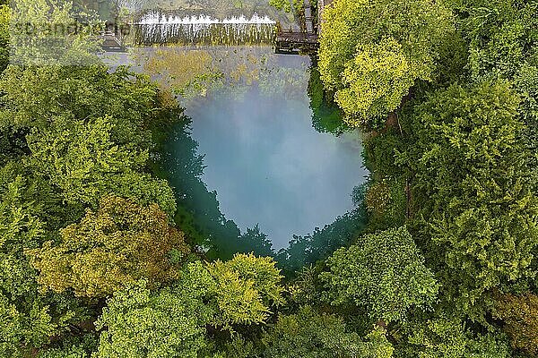 Blautopf Blaubeuren  source of the River Blau in a landscape with forest. Karst spring  geotope and geopoint of the UNESCO Swabian Alb Geopark  tourist attraction. The popular excursion destination is now being thoroughly renovated and will therefore be closed to visitors until the end of 2028. Drone photo. Blaubeuren  Baden-Württemberg  Germany  Europe