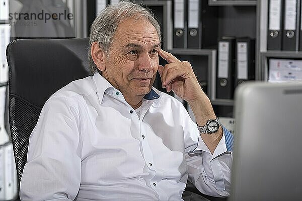 Smiling elderly man in a white shirt sitting at a desk