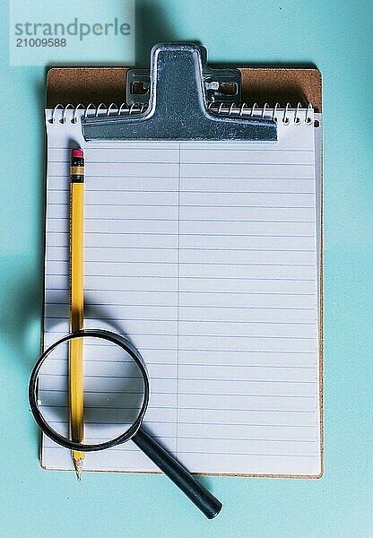 Notepad with pencil and magnifying glass on isolated background. Note book with magnifying glass and pencil on clipboard