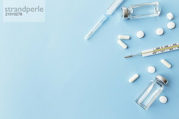 Medicine treatment  vaccination concept. Thermometer  vaccine bottles  injection  syringe  pills on blue background.