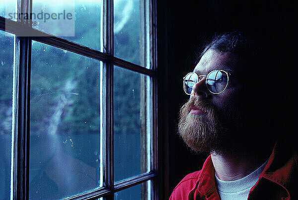 A bearded man looks out a window  Alaska  USA.