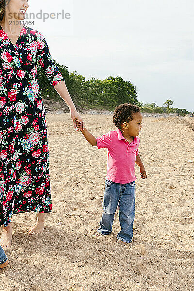 Toddler diverse racially holding moms hand on beach in lake