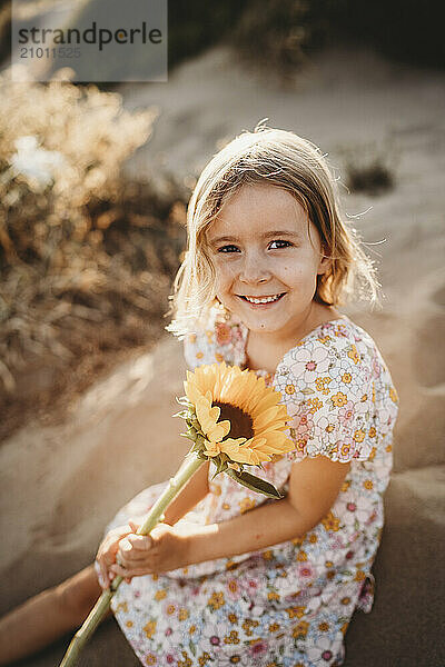 Little girl holding sunflower at beach on summer evening sunset