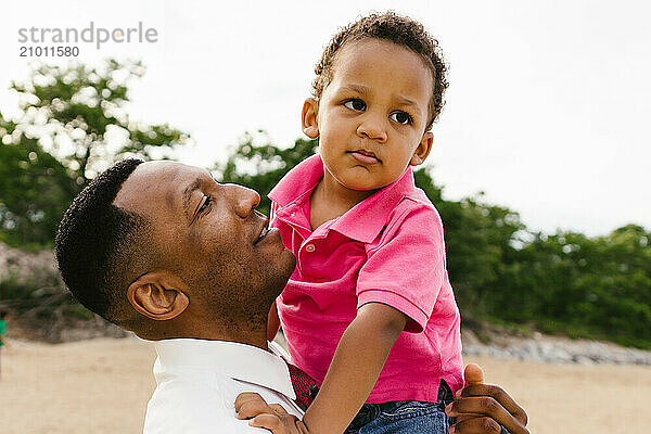 Black father happy holds his toddler son on the beach