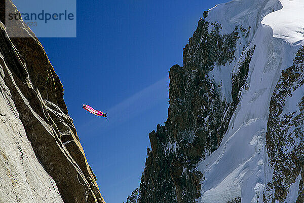 Person Flying In A Bright Red-and-white Wingsuit Between Two Mountains