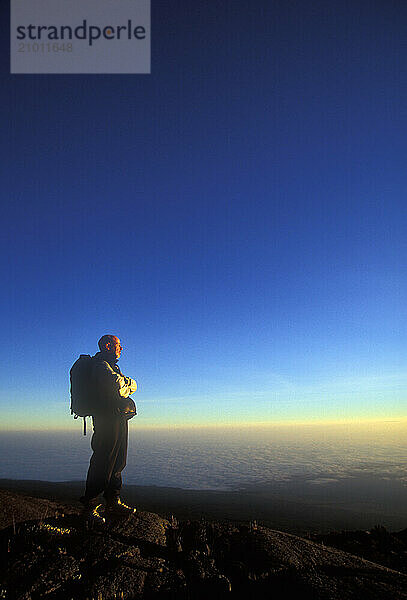 A man stands alone at sunrise as he looks down to the Tanzanian plains below Mount Kilimanjaro.