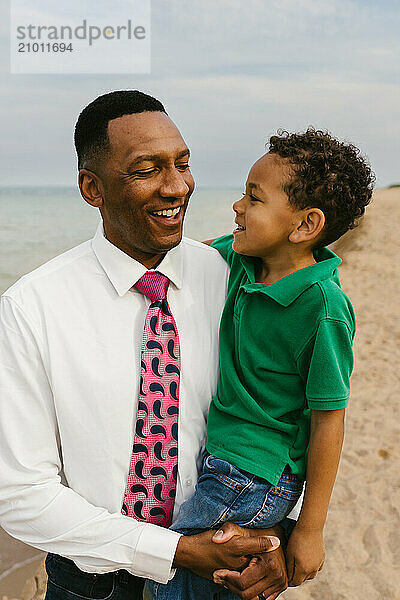 Black father and son laugh together on beach next to lake