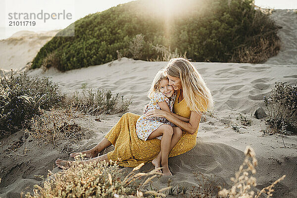 Happy mother and daughter smiling hugging at beach summer sunset