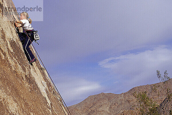 A young girl bravely climbs a cliff side.