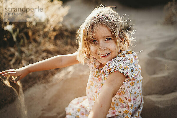 Little girl playing with sand at beach on summer evening sunset