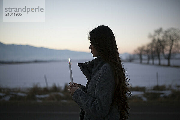 An Asian girl walks with a candle in small town farmland.