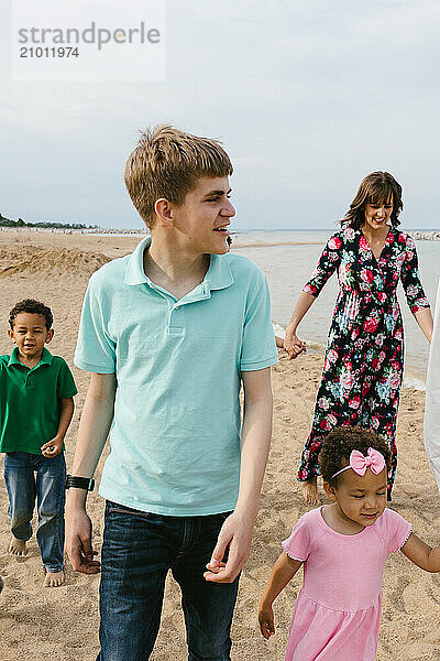 Tween boys walks and smiles with family along beach shore