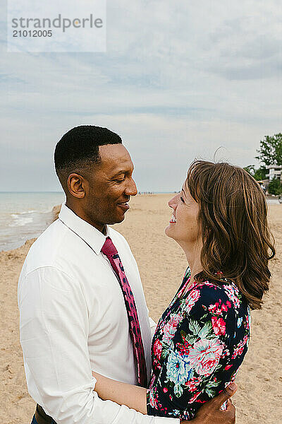 Black husband and white wife smile at each other on beach