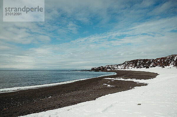 Snowy Djúpalónssandur black beach with ocean and blue sky in Iceland.