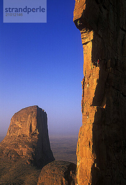 Two men climb one of the sandstone towers that is part of the Hand of Fatima in the Sahara Desert  Mali  West Africa.