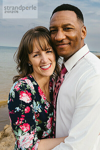 Multi racial couple smile together on waterfront beach