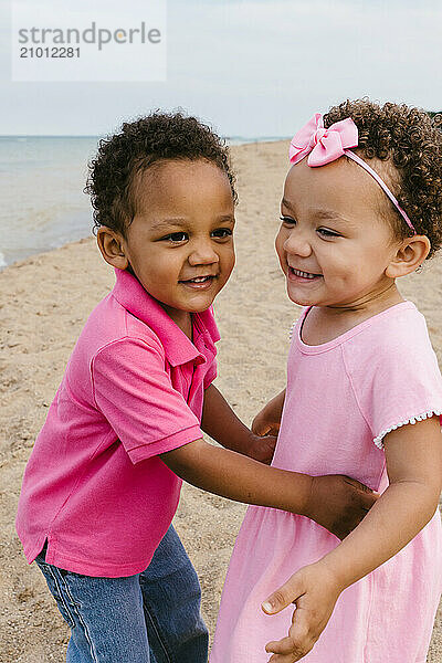 Twin toddler brother and sister laughing together on the beach