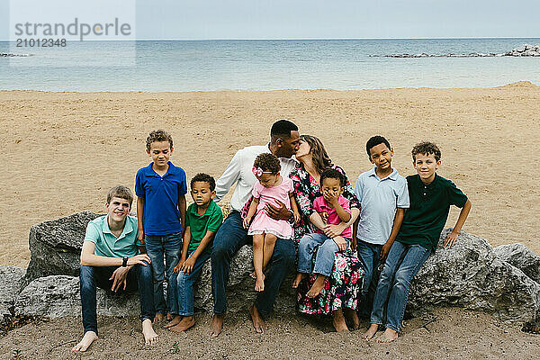 Mom and Dad of large family kiss on beach with kids around them