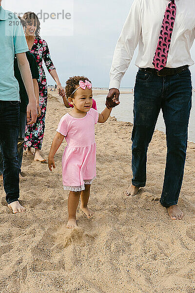 Toddler multi racial girl walks on beach with father and family