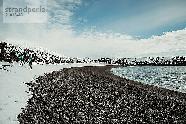 Brother walking on a black beach with ocean and blue sky in Iceland.