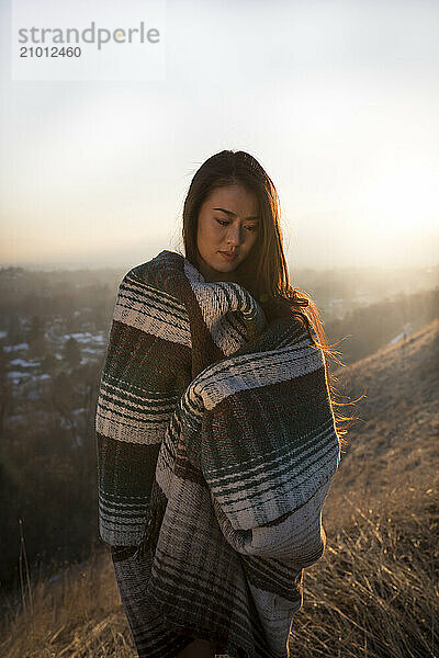 An Asian girl poses in a blanket at sunset over small town.