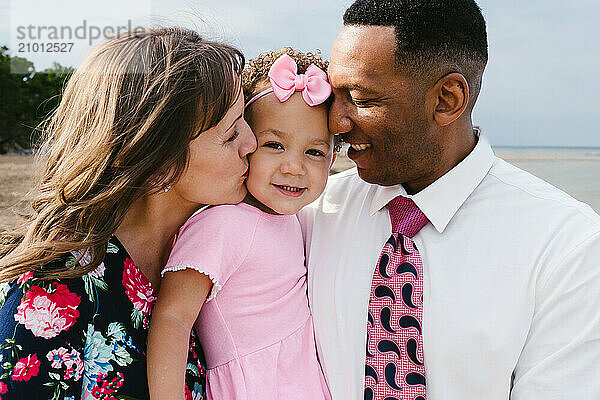 Multi racial mom and dad hold toddler girl close and love