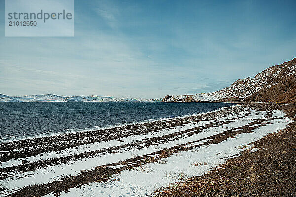 Snowy Djúpalónssandur black beach with ocean and blue sky in Iceland