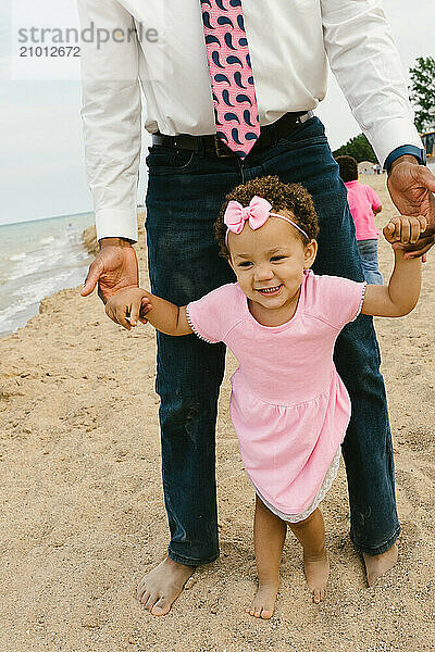 Daughter holds father's hands on beach in summer barefoot