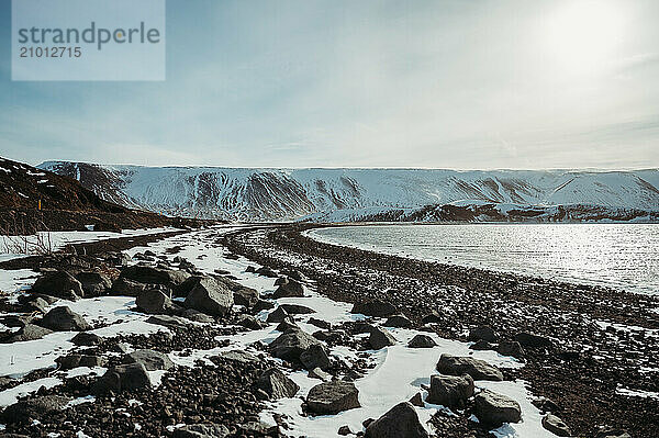 Snowy Djúpalónssandur black beach with ocean and blue sky in Iceland.