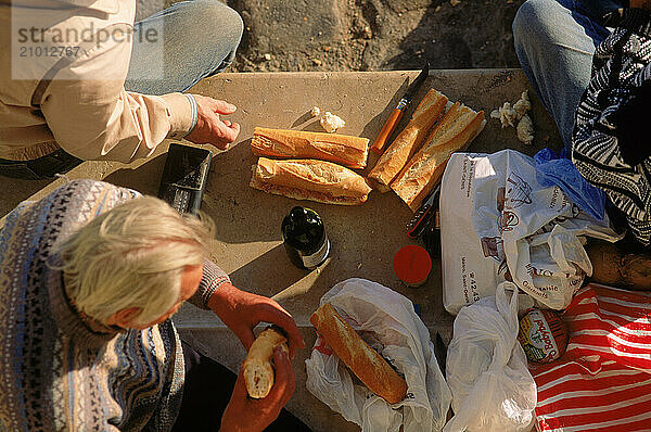 Men eating bread and wine at a picnic.