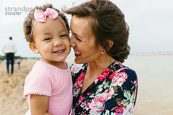 Diverse Mom and daughter smile together on beach