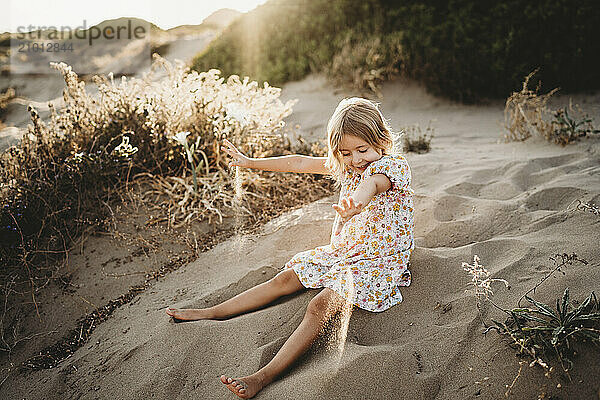 Little girl playing with sand at beach on summer evening sunset