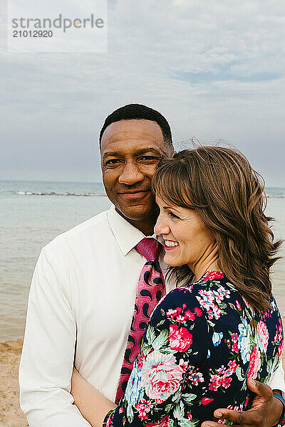 Black man hugs wife and smiles on beach by the lake