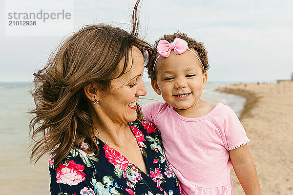 Mother and daughter laugh and smile together on beach