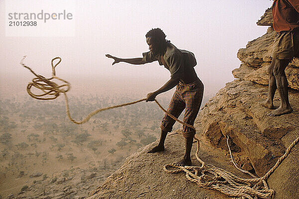 Man throws rope from top of cliff  Mali