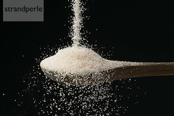 A studio photo of fine himalayan sea salt pouring down on a wooden spoon set against a black background