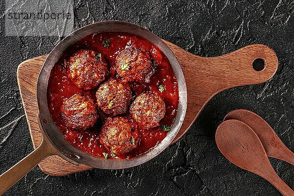 Meatballs. Beef meat balls  overhead flat lay shot in a pan  with parsley and tomato sauce  on a black background  with wooden spoons  Food photography