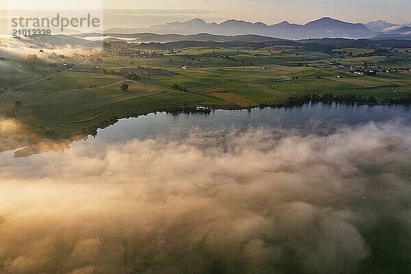 Aerial view of a lake in front of mountains in the morning light  fog  autumn  Riegsee  view of Benediktenwand and Jochberg  Alpine foothills  Upper Bavaria  Bavaria  Germany  Europe