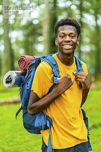 Vertical portrait of a young african man having a walk with a backpack through beautiful nature